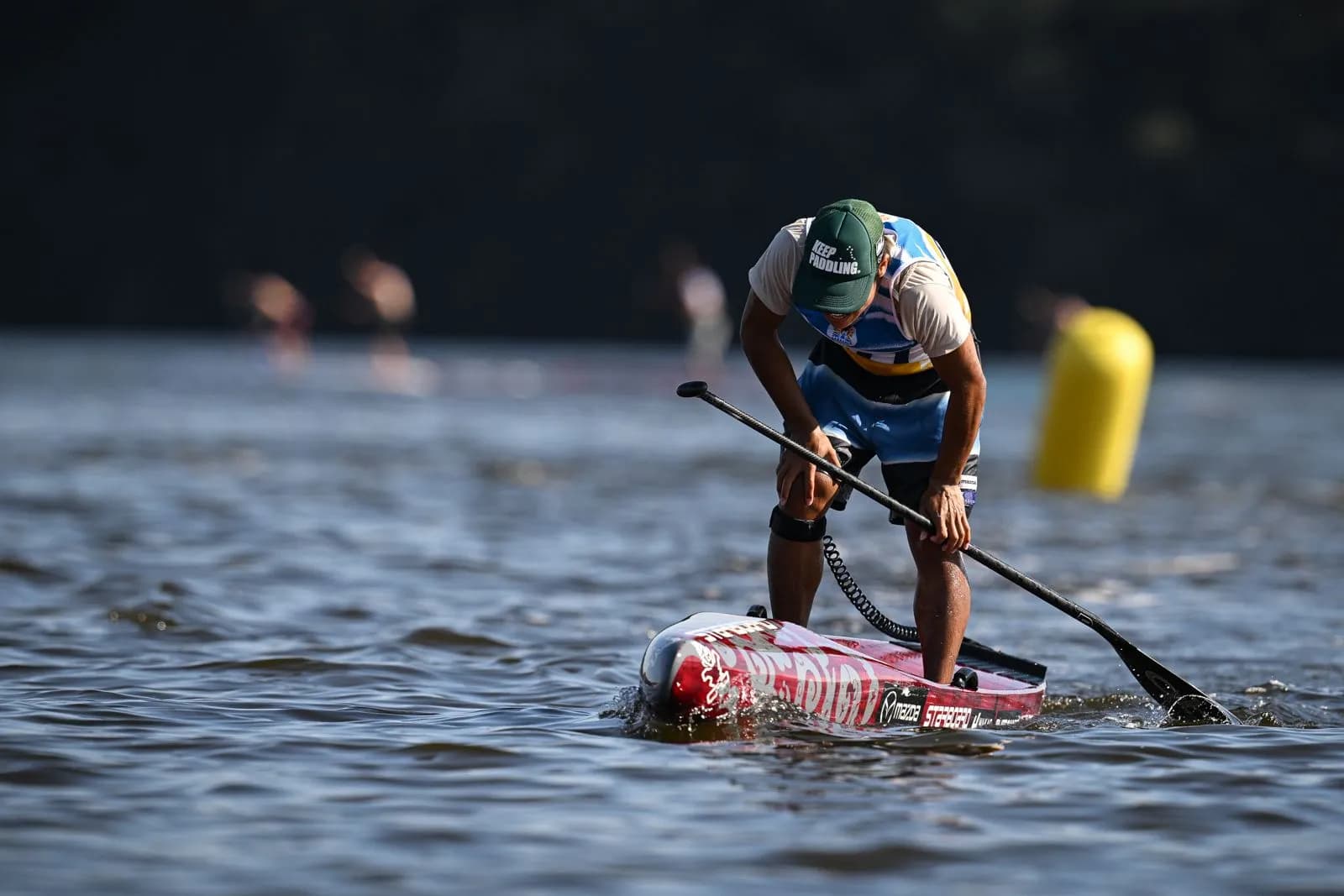 Гонка на SUP на чемпионате мира в Сабаудии: спортсмен гребёт низко над водой мимо буя, на заднем плане другие участники